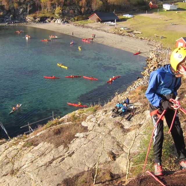 Elever som rapellerer med kajakker i bakgrunn